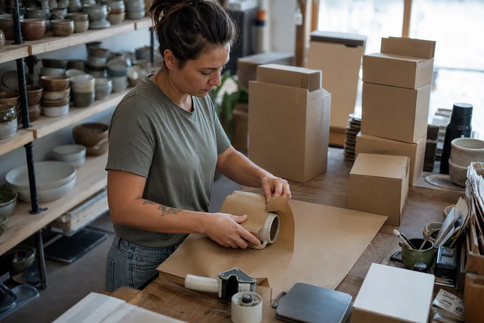 Online ceramics store owner wrapping orders at a packing bench