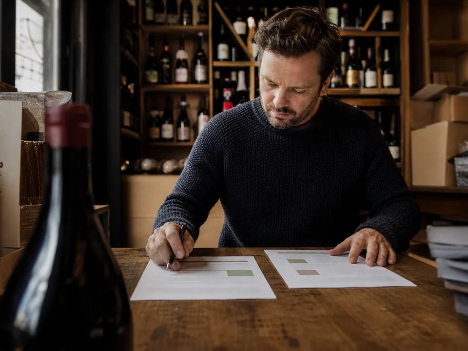 Wine shop owner comparing two printed proposals at a wooden table